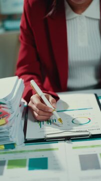 Professional businesswoman reviewing financial data, studying pie chart and bar graph on clipboard near scattered documents, concentrating on strategic business metrics