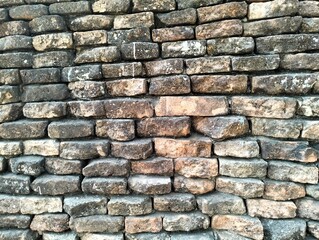 In the picture is a picture of a brown-gray ancient brick wall. It is a wall made of bricks and arranged in rows to form a wall that is old and ancient. The color of the edge of the wall is starting t