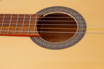 Obraz premium A fragment of a classical acoustic guitar is shown in close-up. Particular attention is paid to the soundhole with a decorative ring around it. The guitar's body is light brown, glossy.