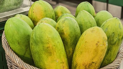 Close up of fresh green and yellow papayas in a woven basket display
