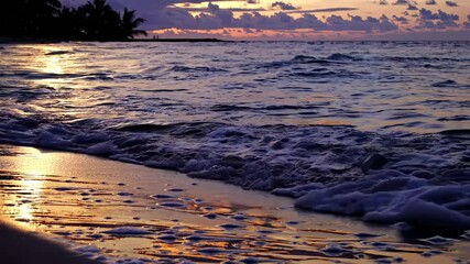 A serene beach sunset video with gentle waves lapping the shore. Captured from a low angle, highlighting the vibrant sky and reflective water.