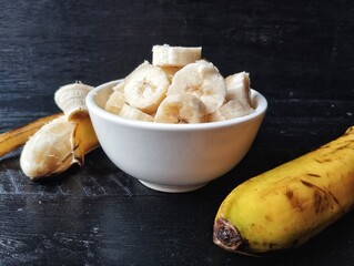Fresh slice bananas in bowl on black wooden table background 