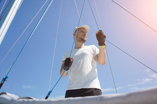 Male captain on deck of sailboat opening sails pulling the rope