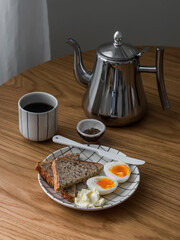 A simple and delicious breakfast - boiled egg, whole grain bread, butter, coffee on a wooden table