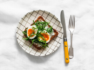 Sandwich with cream cheese, boiled egg, arugula on a light background