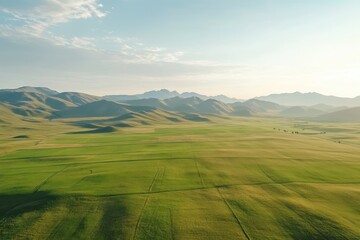 Fototapeta premium Vast green fields and rolling mountains under a clear sky create a stunning landscape in the countryside, Squares of green fields, with rolling mountains in the distance, aerial shot