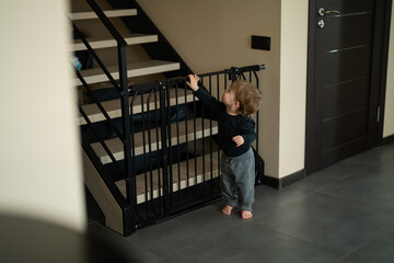 Small baby boy safely can't access stairs because he is protected by stair fence gate. Baby safety stair gate only for parental access