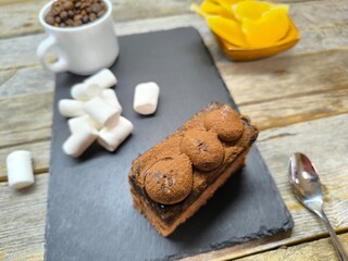 tender juicy tiramisu cake lies on a granite board next to pineapple pieces, marshmallows and a white cup with coffee beans