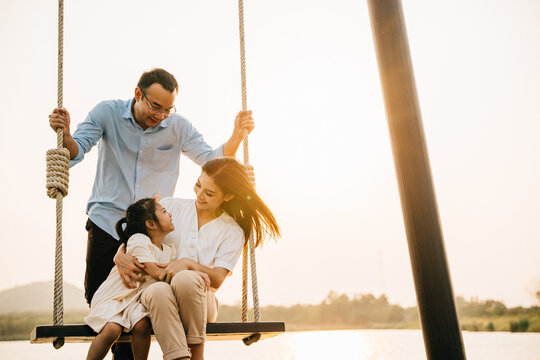 A family having a vacation in a nature setting, with the children swinging on a swing in a beautiful park at sunset, feeling the playful and cheerful spirit of the outdoors, Happy Family Day