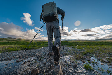 A tourist traveler with a backpack on his back and trekking poles in his hands walks through the water. A man in hiking shoes walks on the water, view from below.