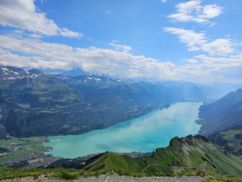 A breathtaking summer photo taken from the summit of Brienzer Rothorn, showcasing the serene beauty of Lake Brienz nestled in the Swiss Alps. The turquoise waters of the lake contrast beautifully with