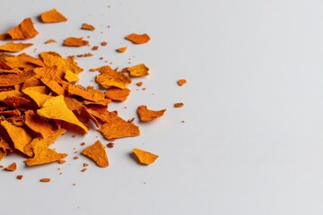 A close-up of dark yellow paprika flakes scattered across a muted white surface, arranged on the top left with a clean, expansive negative space filling the rest of the composition. 