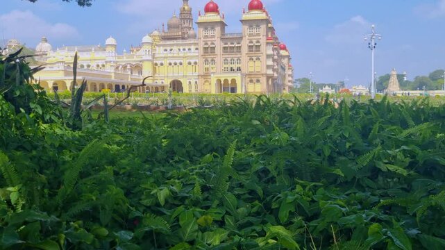 Revealing shot of the Amba Vilas Palace in Mysore, India, elegantly framed by lush green vegetation under a partly cloudy sky