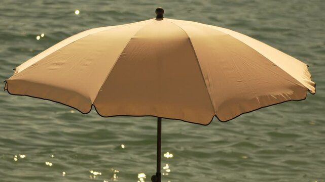 A Single Beige Beach Umbrella Against A Rippling Green Water Background