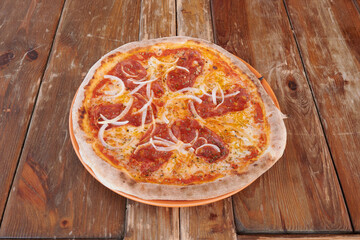 A pizza with pepperoni and onions on top sits on a wooden table