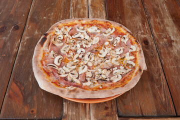A pizza with mushrooms and ham on it sits on a wooden table