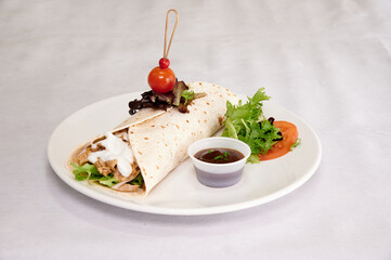 A plate of food with a burrito and a tomato on top