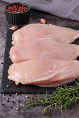 Fresh chicken breasts ready for cooking on a dark slate board with herbs and spices