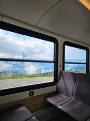 A unique and captivating photo taken inside a train on Mount Rigi, Switzerland, offering a scenic view of the stunning Swiss Alps. The image features the comfortable and cozy interior of the train, wi