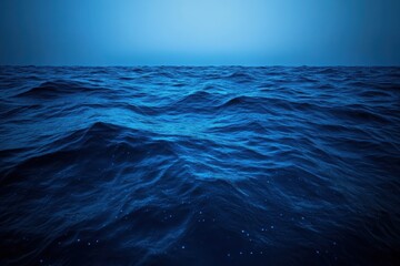 Fototapeta premium An abstract view of a glowing deep-sea surface with a rich navy-blue color, illuminated by scattered bioluminescent dots and swirling water patterns. 