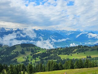 A stunning summer view from Mount Rigi, often referred to as the "Queen of the Mountains," offering panoramic vistas of the Swiss Alps and surrounding lakes. This image captures the lush green meadows