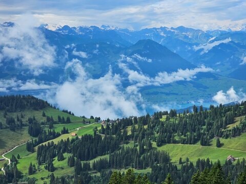 A stunning summer view from Mount Rigi, often referred to as the "Queen of the Mountains," offering panoramic vistas of the Swiss Alps and surrounding lakes. This image captures the lush green meadows