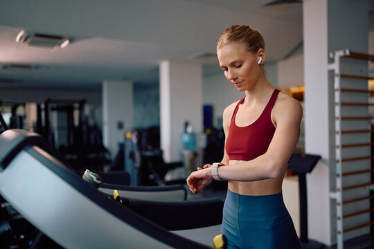 Athletic woman using fitness tracker while working out on treadmill in gym.