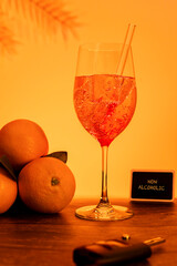 Glas mit orangefarbenem Getränk, im Vordergrund ein Autoschlüssel und im Hintergrund Orangen und ein Schild mit der Aufschrift NON ALCOHOLIC zu sehen, vertikal        