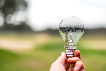 Hand holding a light bulb against a blurred natural background symbolizing renewable energy,...