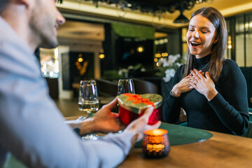 Boyfriend gives his girlfriend a gift on a romantic dinner date in a restaurant.