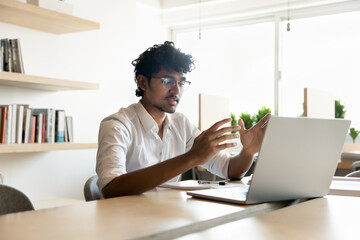 Young 18s Indian student guy speaks through videocall application on computer, studying online,...