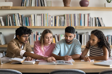 Group of four students gathered around table in library, engaged in collaborative study session, working together on project, researching topic, or preparing for academic assignment. Higher education