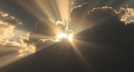 Sun rays piercing through dark clouds background. Dramatic beams of golden light breaking through