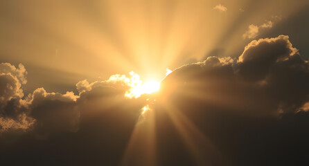 Sun rays piercing through dark clouds background. Dramatic beams of golden light breaking through