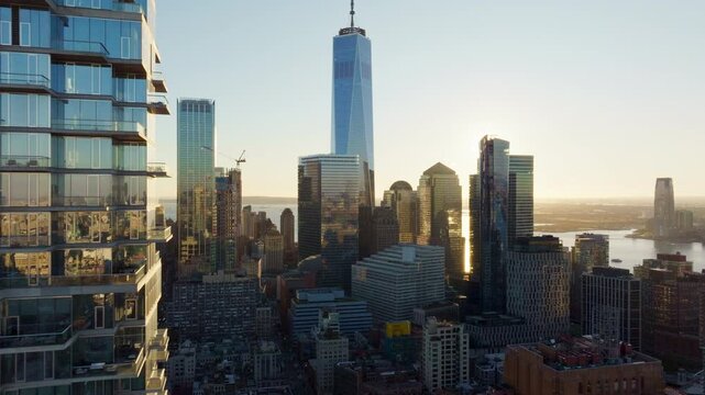 Sunlight shines from behind One World Trade Center in Lower Manhattan, illuminating surrounding buildings in New York City's Financial District during sunrise