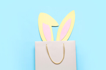 Shopping bag with paper Easter bunny ears on blue background
