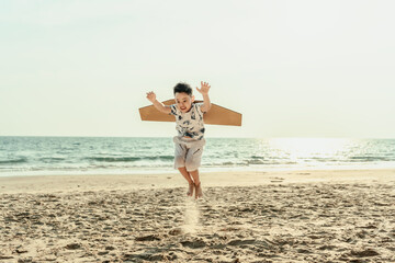 Wearing paper airplane wings makes a boy feel like they are traveling and jumping on the beach happily while on a holiday, travel, long weekend, summer, or any other holiday.