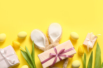 Bunny ears with Easter eggs, tulip flowers and gift boxes on yellow background