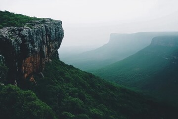 Fototapeta premium Misty morning view of lush canyon landscape with steep cliffs dense greenery