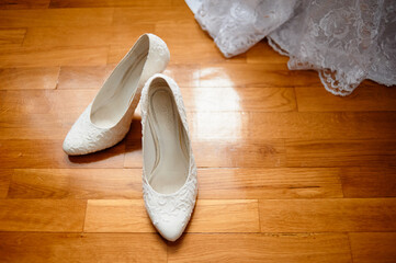 Elegant White Wedding Shoes on Wooden Floor Near Lace Gown..