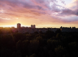 Fototapeta premium Sunset Silhouetting Urban Residential Buildings with Atmospheric Sky and Forest..