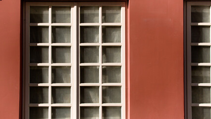  A symmetrical window design, featuring a contrast between light and shadow on a red facade.