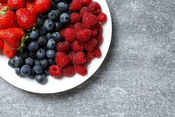 Different fresh ripe berries in bowl on gray table, top view