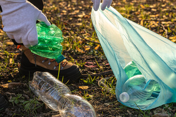 A volunteer man collecting plastic trash in the park and holding a blue garbage bag. Pick up plastic garbage. Plastic bottles left on the ground. To litter. Enviroment protection, ecology concept.