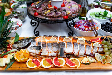 Deliciously prepared whole fish garnished with citrus fruits, served at a vibrant feast surrounded by fresh salads and appetizers