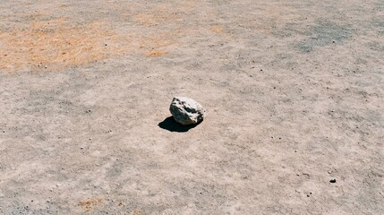 Lone rock on barren land, casting shadow, desolate landscape