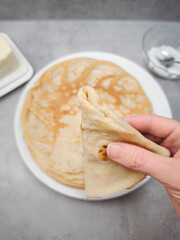 Woman holding folded crepe above plate of crepes for pancake day, shrove tuesday, maslenitsa or breakfast