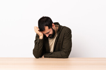 Caucasian man with beard in a table with headache.
