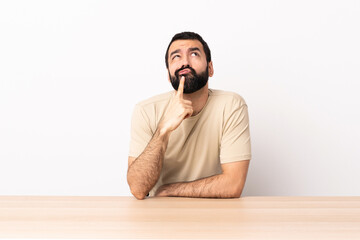 Caucasian man with beard in a table having doubts while looking up.