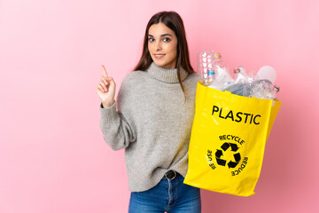 Young caucasian woman holding a bag full of plastic bottles to recycle isolated on pink background...